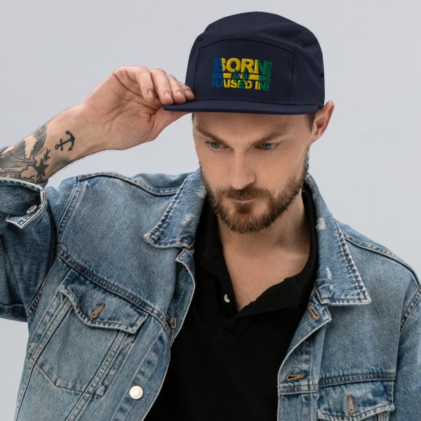 A man in denim jacket and jeans holding his hat.